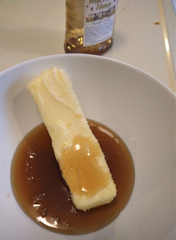 a stick of butter with honey in a white bowl