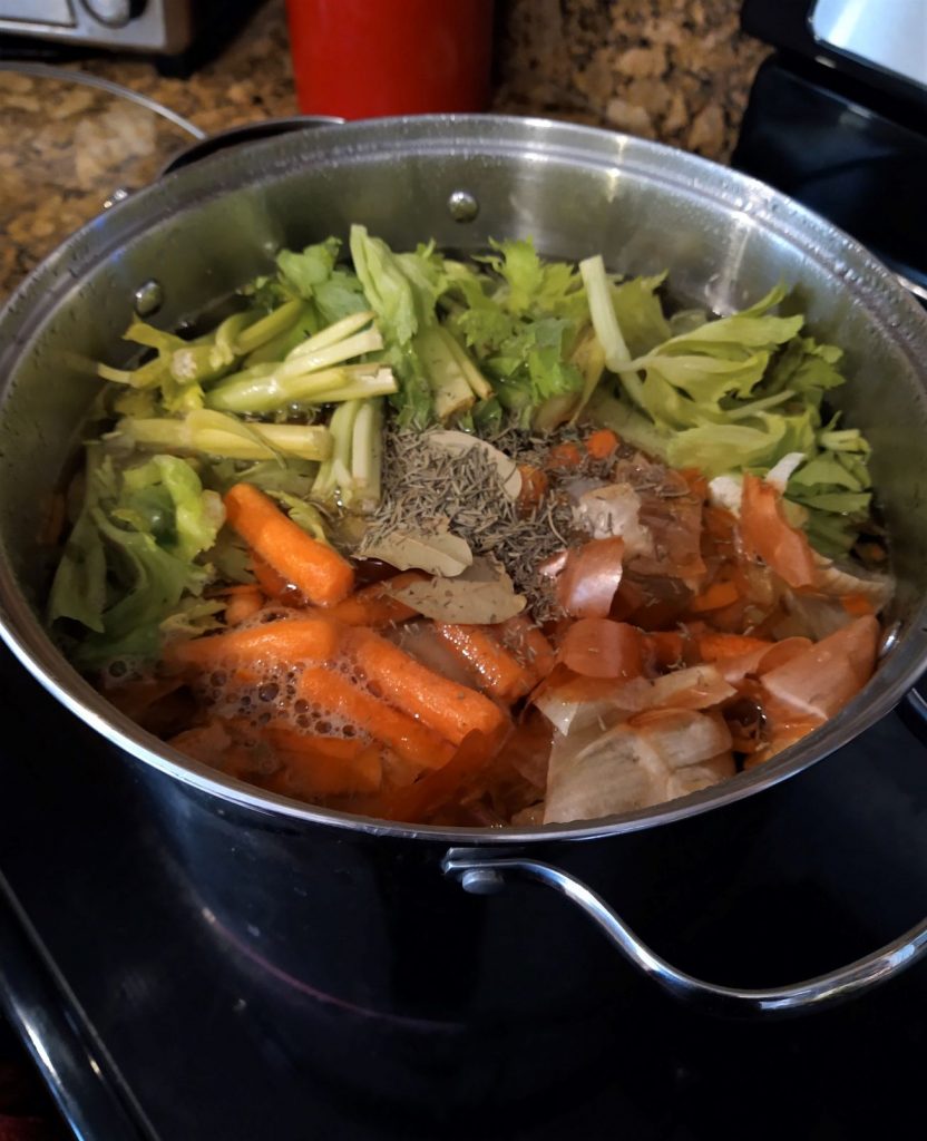 large metal pot full of water, carrots, celery, onions, chicken bones, and herbs