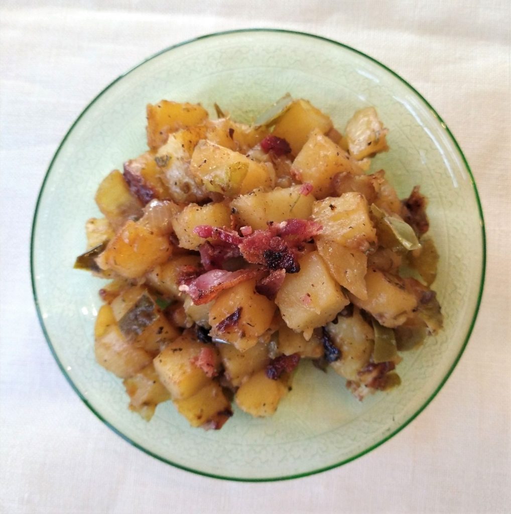 cooked potatoes with bacon on a green plate and white background