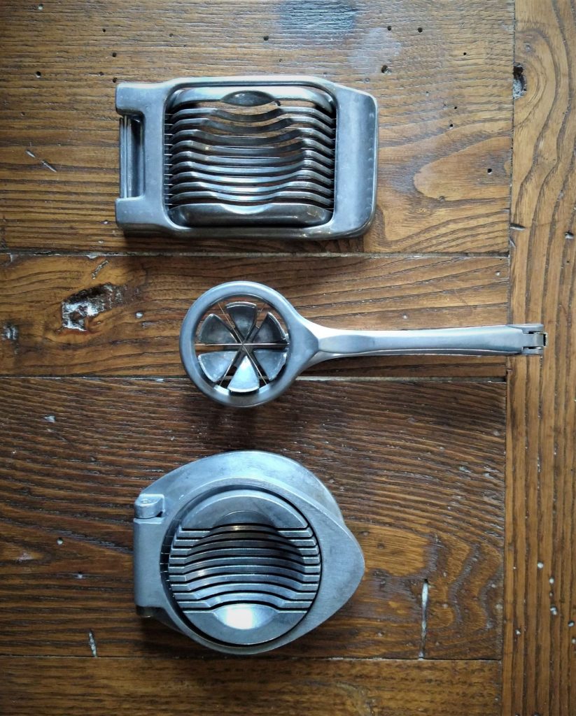 three vintage aluminum egg slicers on a wooden surface