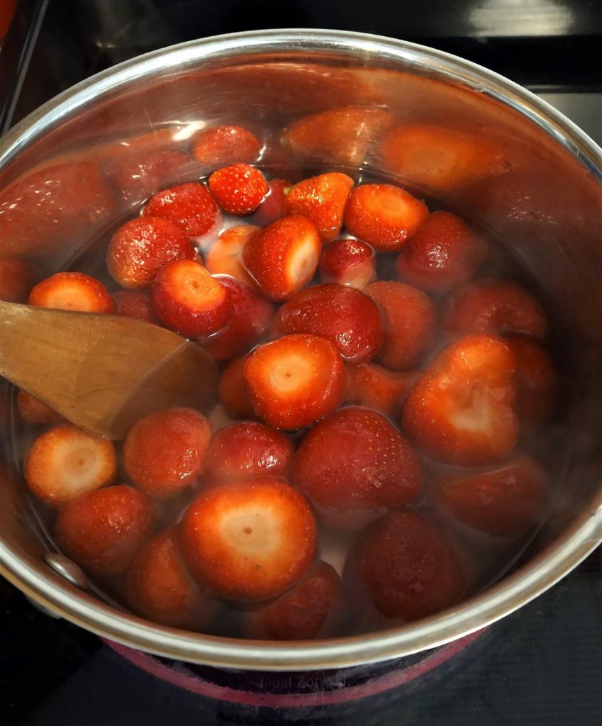 silver pot full of strawberries cooking in syrup being stirred by a wooden spoon