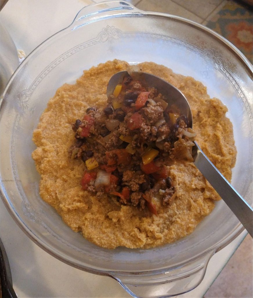 cornmeal mush being topped with a spoonful of meat casserole filling to make tamale pie special
