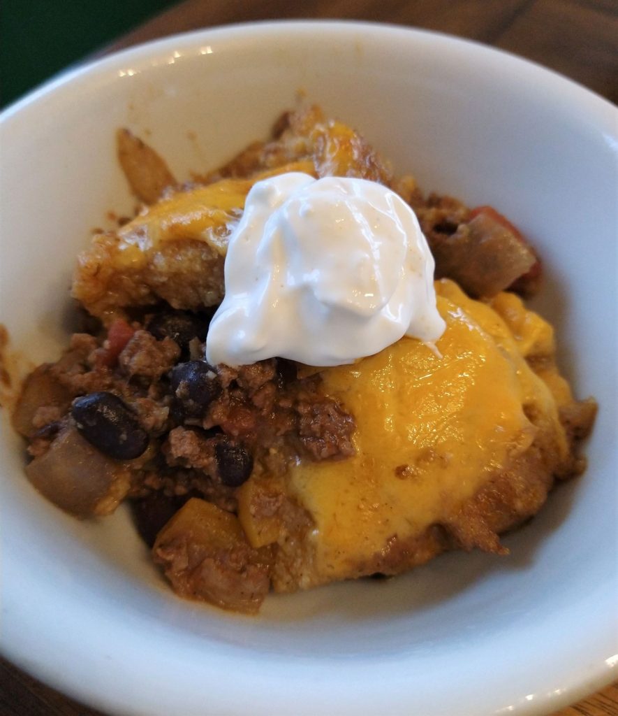 tamale pie special casserole in a white bowl topped with sour cream