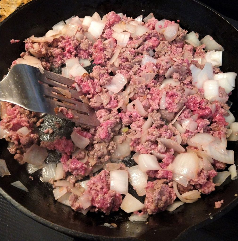 ground beef being browned with chopped onion in a cast iron skillet