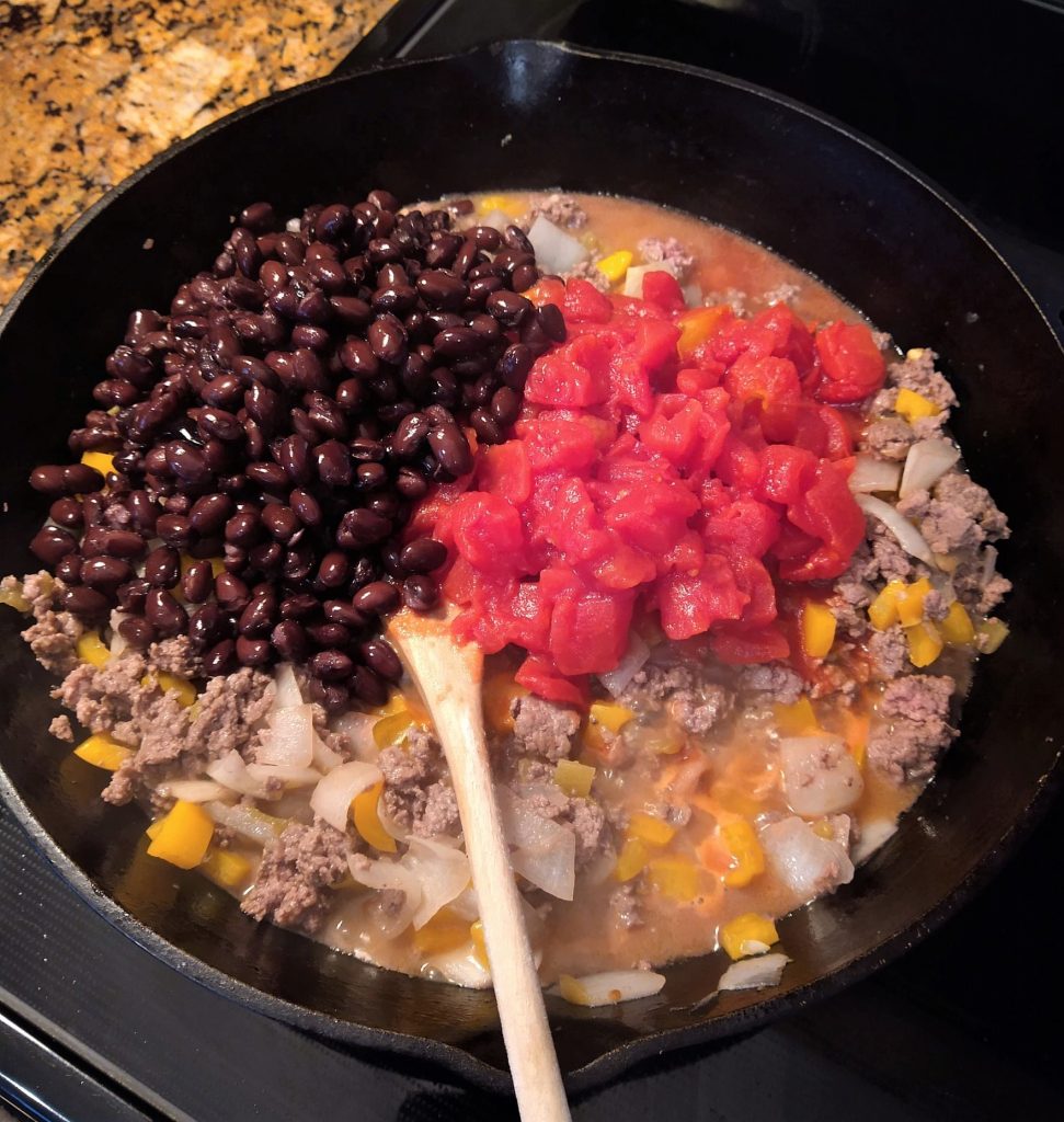 ground beef and onions with black beans, canned diced tomatoes, and diced yellow peppers in a cast iron skillet