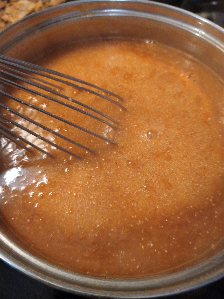 a whisk stirring cooking cornmeal in a silver pot