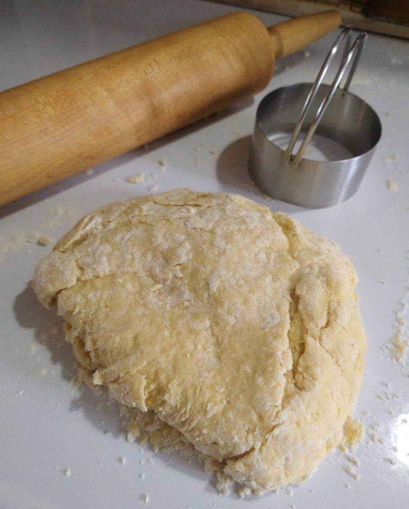 shortcake dough, rolling pin, and a biscuit cutter on a table surface