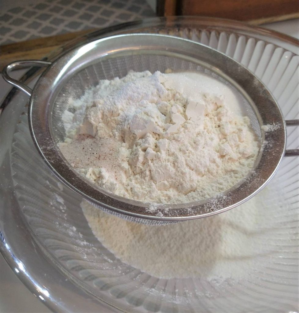 flour mixture in a sieve sitting atop a glass bowl