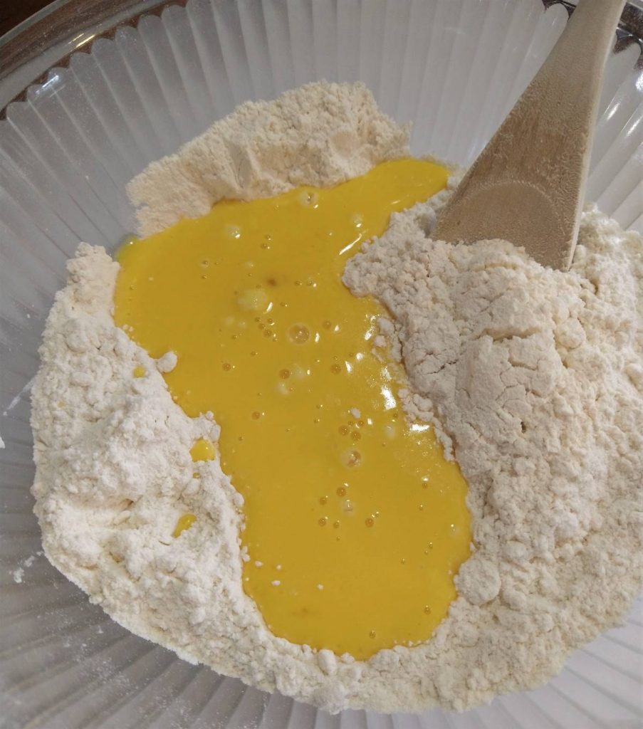 flour mixture with yellow egg mixture in a glass bowl and wooden spoon
