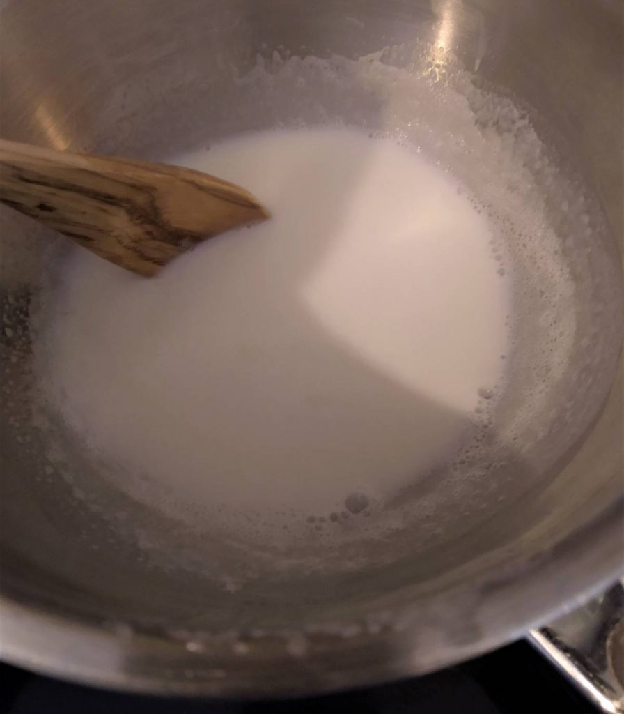 milk being scalded in a double boiler with a wooden spoon for stirring
