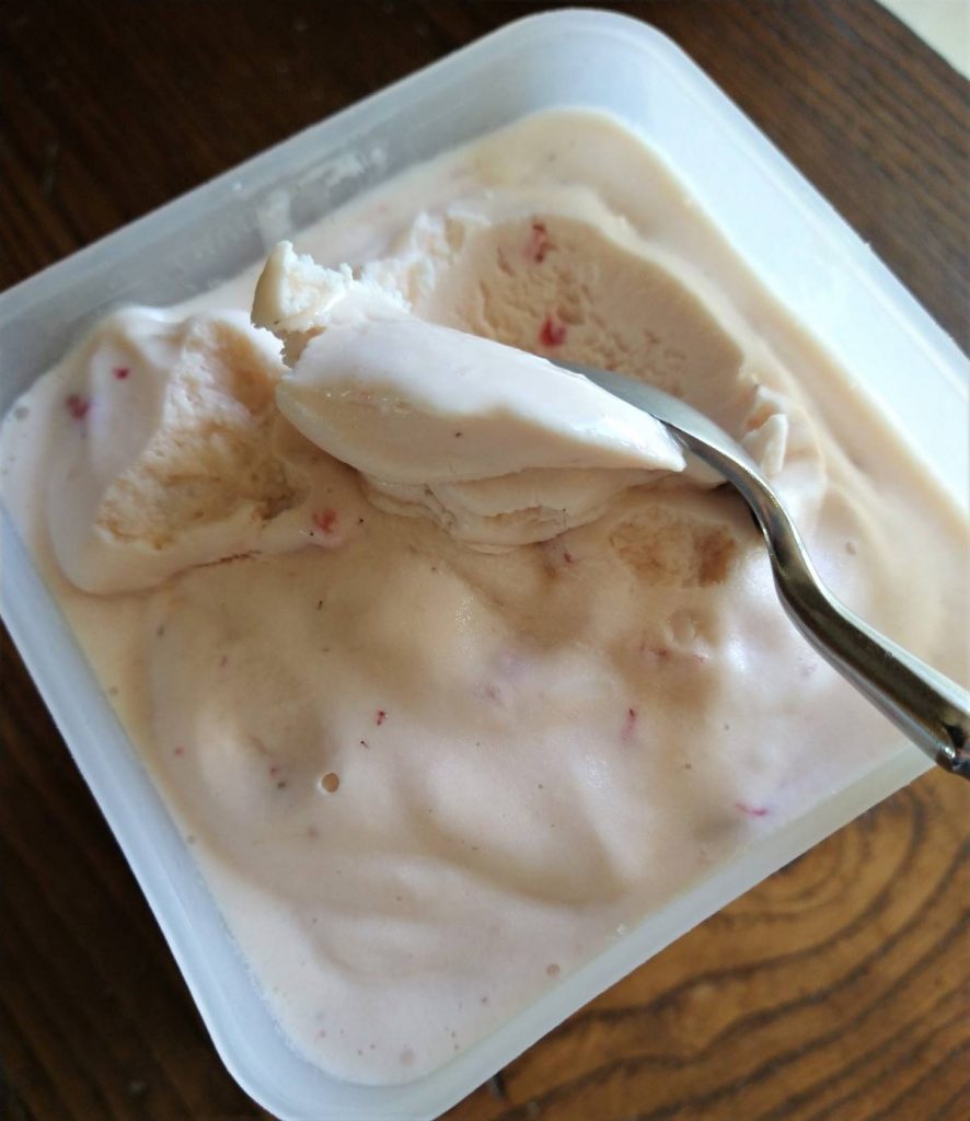 metal spoon scooping strawberry ice cream from a plastic container