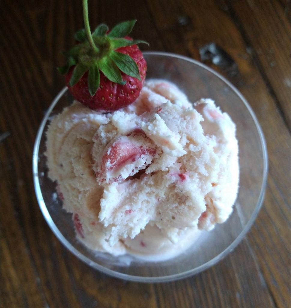glass dish of strawberry ice cream with a fresh strawberry garnish