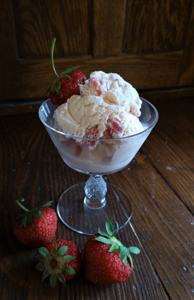 strawberry ice cream in a glass dish with fresh strawberries in foreground