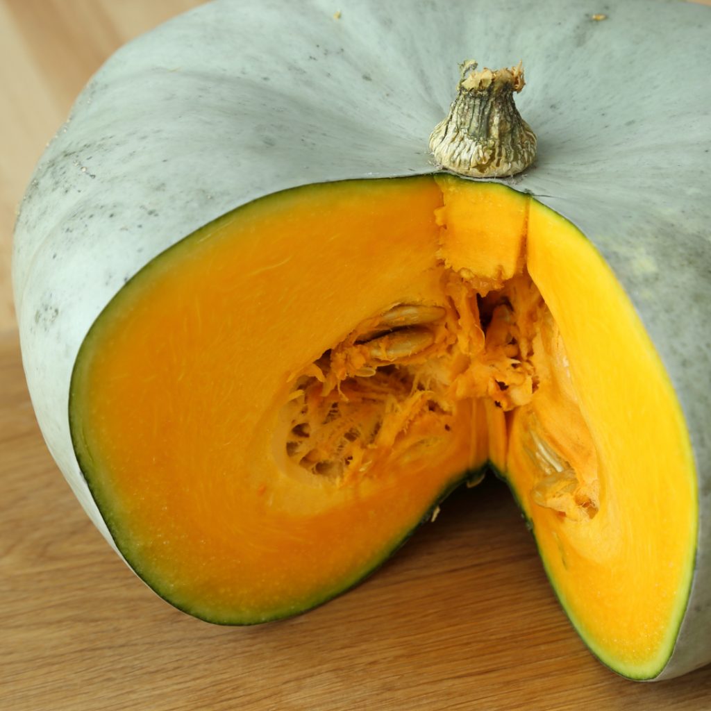 blue hubbard squash cut open to reveal orange insides and seeds sitting atop a wooden table