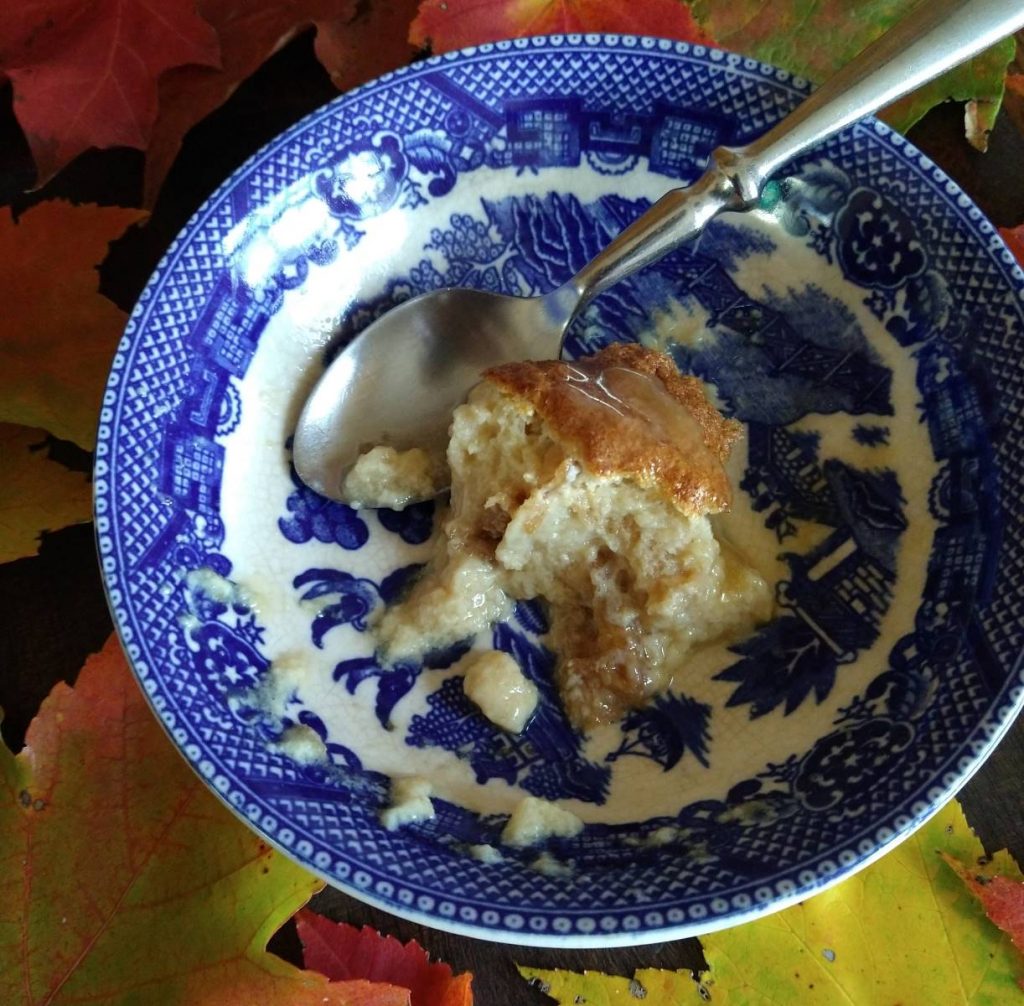 maple bread pudding with butterscotch sauce in a blue and white china dish surrounded by colorful autumn leaves