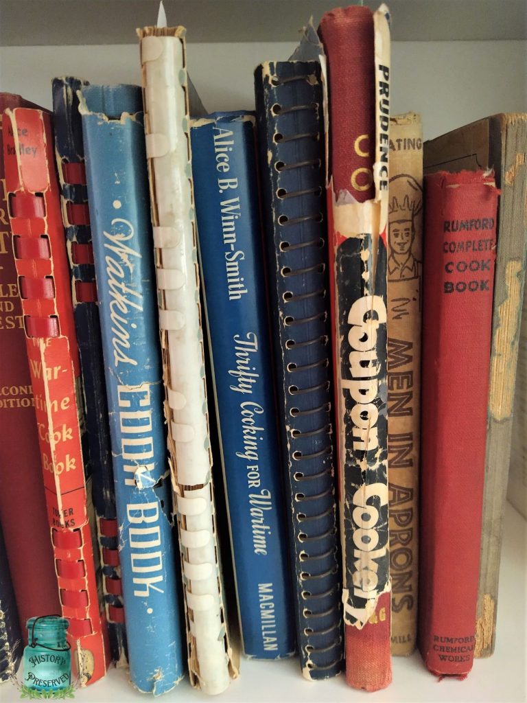various vintage cookbooks stand upright on a bookshelf, some with shabby covers