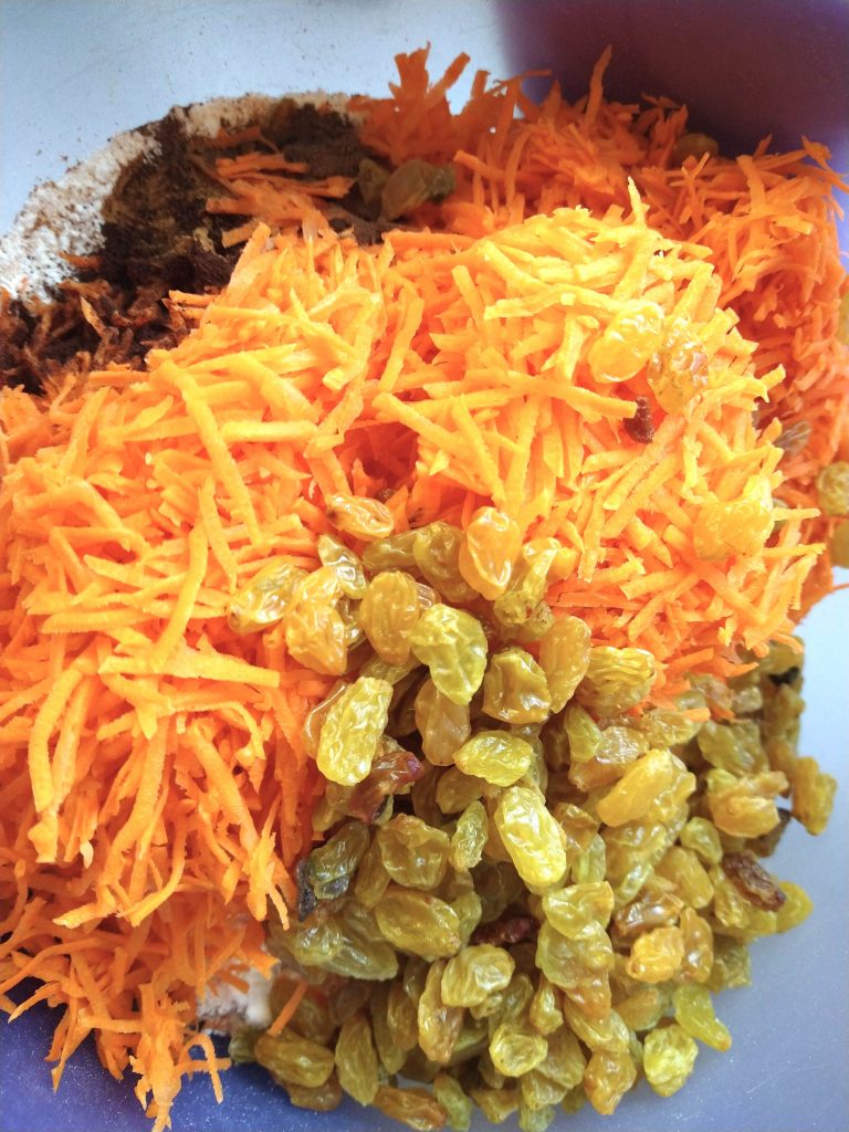 a pile of the recipe's ingredients sit in a bowl: shredded carrots, golden raisins, flour, spices and everything else