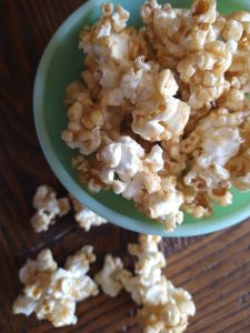 a glass bowl sits on a wooden surface filled with caramel popcorn
